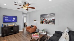 Ein modernes Wohnzimmer mit Flachbildfernseher, Deckenventilator, Sofa, Couchtisch und einem Gemälde an der Wand.