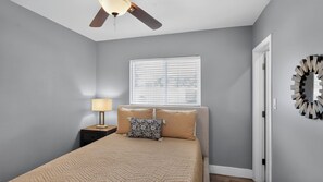 Ein Schlafzimmer mit Bett, Nachttisch, Lampe, Deckenventilator, Fenster und Tür.