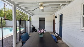 Eine überdachte Terrasse mit Tisch und Stühlen, einem Deckenventilator und Blick auf einen Swimmingpool.