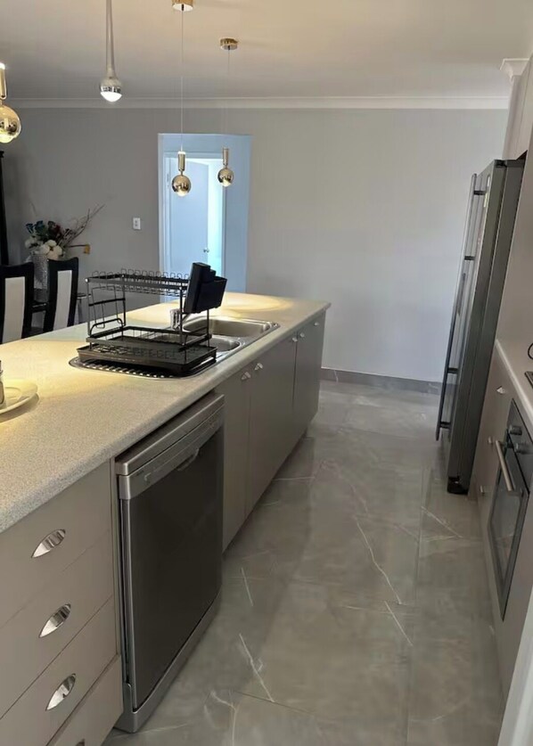 A modern kitchen with a large island, stainless steel appliances, and pendant lighting. - Cozy Family home (Caversham)