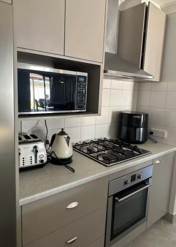 Una cocina moderna con microondas, tostadora, hervidor, estufa a gas, cafetera y horno.