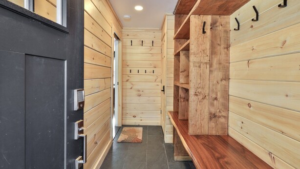 Een houten interieur met een bank en planken, een deur met een hendel, en een betegelde vloer.