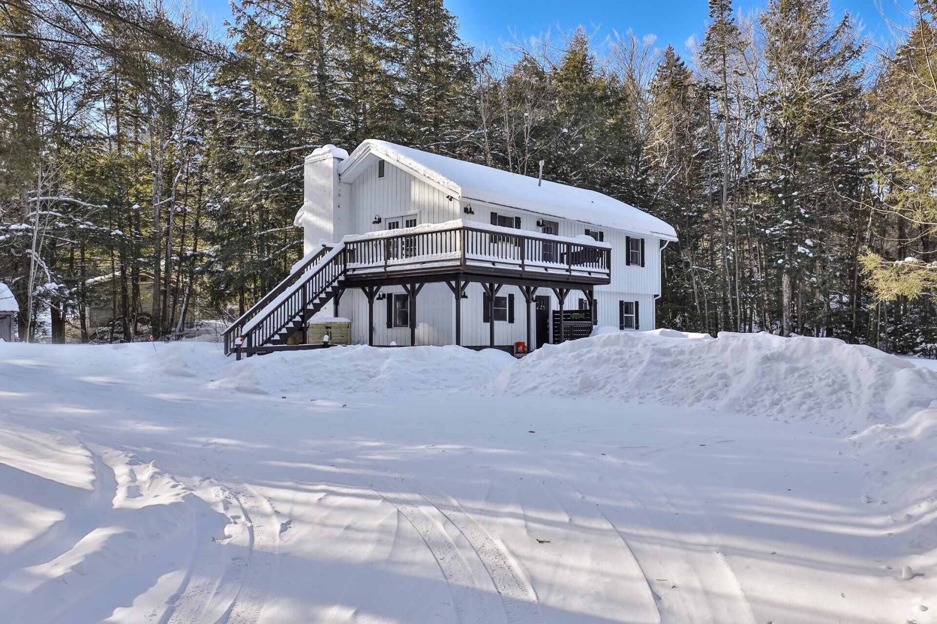 A white wooden cabin with a balcony, surrounded by snow-covered trees.