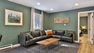 A modern living room with a leather sectional sofa, a wooden coffee table, and two framed artworks.