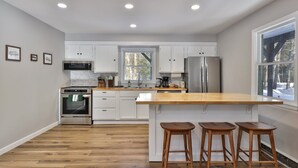 Een moderne keuken met witte kastjes, roestvrijstalen apparatuur, een houten aanrecht en een groot raam.