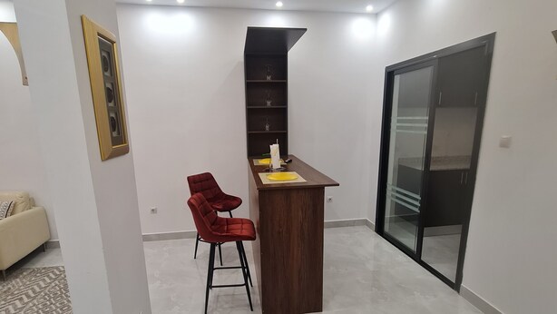 Una habitación moderna con un escritorio de madera, dos sillas rojas, un aparador de vidrio y un espejo grande.