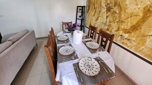 Comedor con una mesa lista para cuatro personas, con platos estampados, un florero con flores y un cuadro abstracto grande en la pared.
