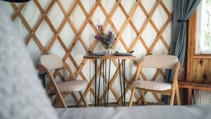 Una habitación con dos sillas de madera, una mesa pequeña con un jarrón de flores y una ventana con cortinas.