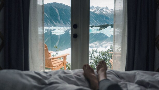 Una cama con vista a un paisaje montañoso a través de una ventana con cortinas.