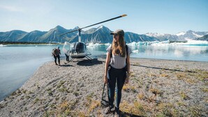 Un helicóptero sobre una costa rocosa con montañas al fondo.