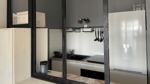 Ett modernt kök med en spegel med svart ram, vita skåp, en inbyggd ugn, ett kylskåp i rostfritt stål och en svart bänkskiva.