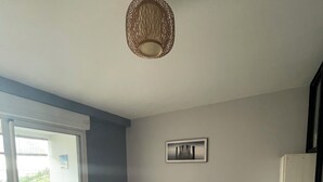 Ett sovrum med en säng, två sängbord, en taklampa, en inramad tavla på väggen och en skjutdörr i glas som leder ut till ett utomhusområde.
