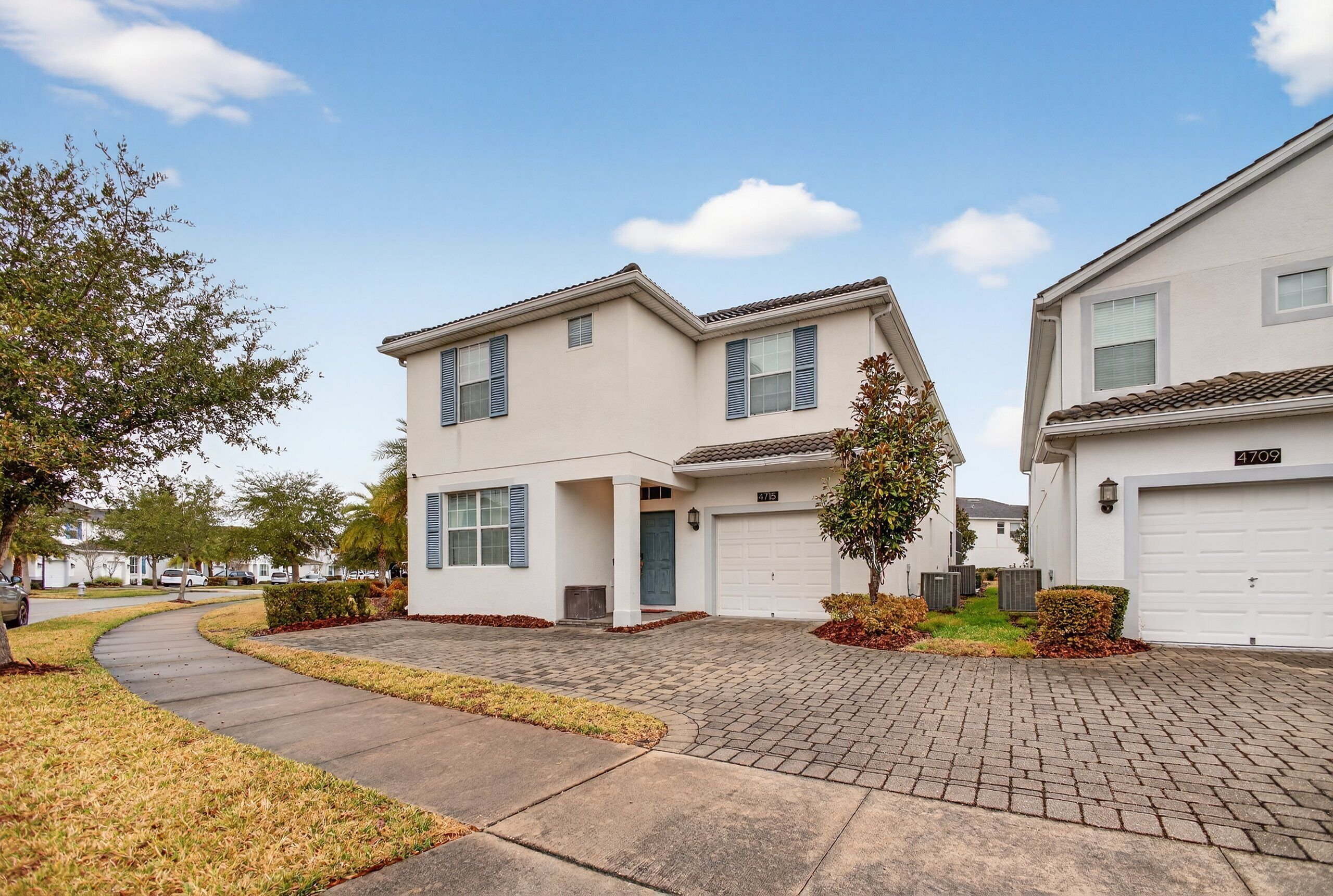 A residential neighborhood with two-story houses, paved driveways, and a clear sky.