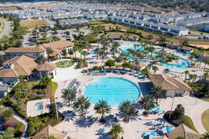 Ovenudblik over en feriepark med en stor central pool, flere mindre pools og talrige liggestole og parasoller.