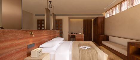 A modern hotel room with a large bed, a wooden headboard, a bedside table with a lamp, and a view of the hallway.