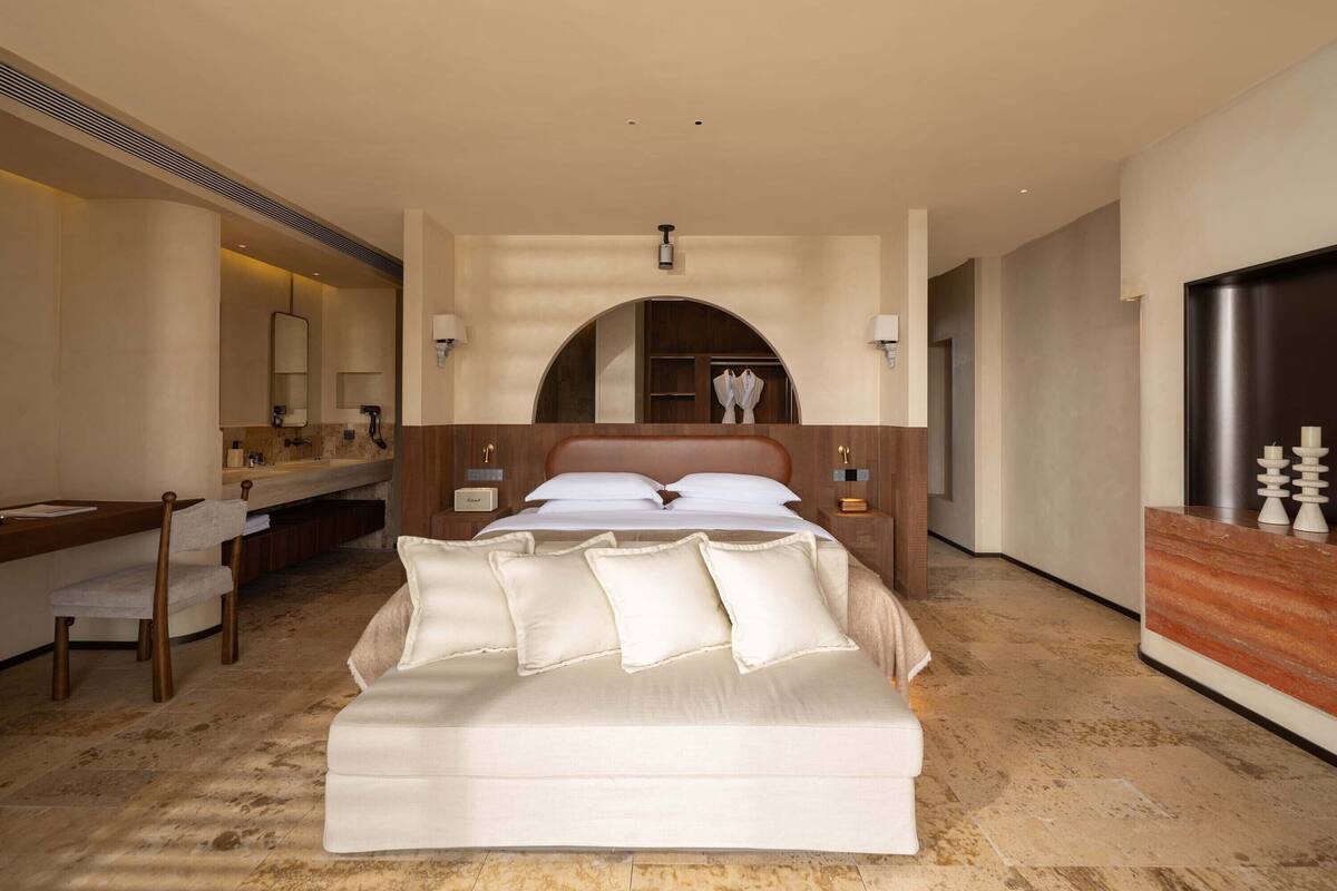 A hotel room with a large bed, a desk with a chair, a vanity with a mirror, and a wardrobe.