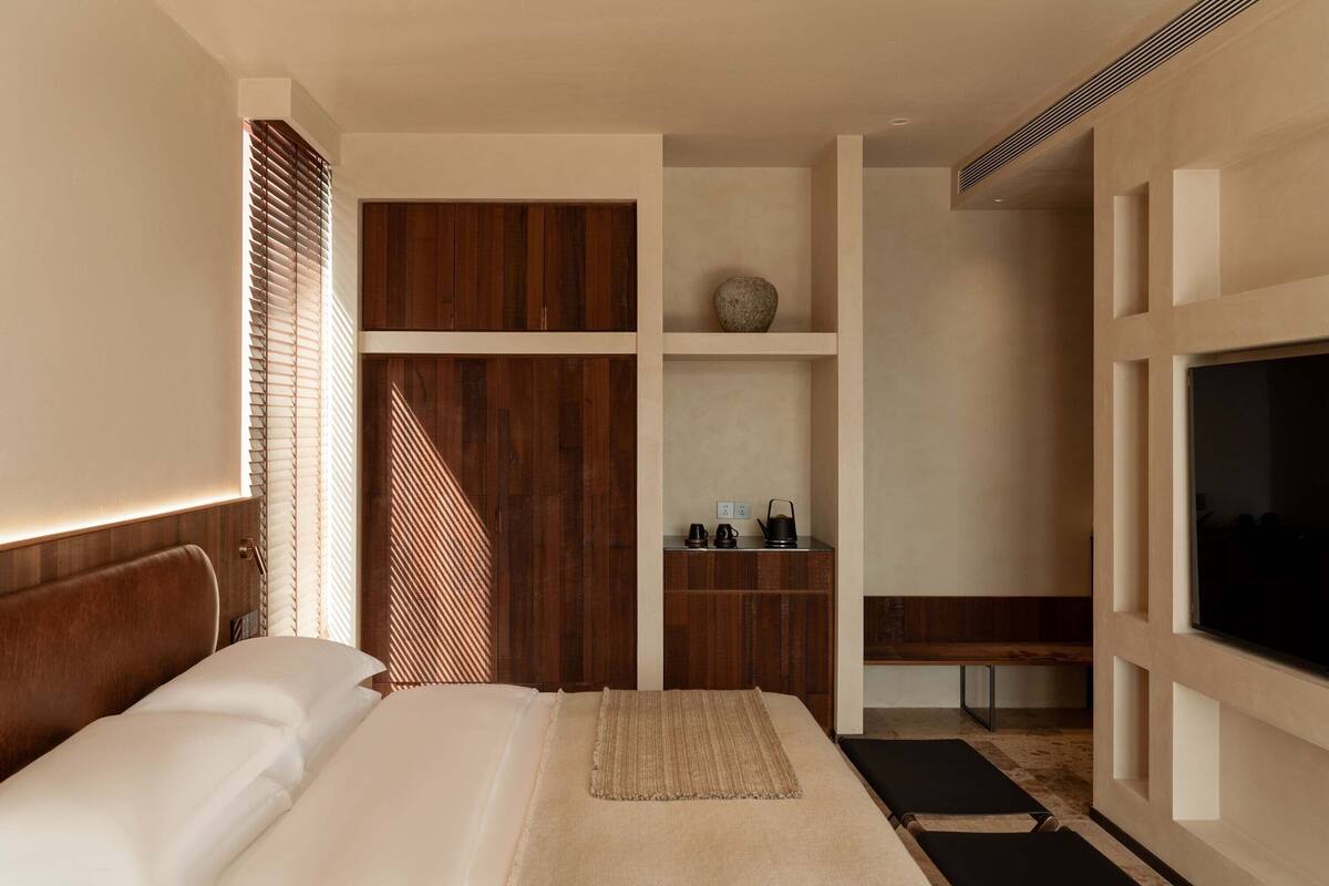 A modern hotel room with a large bed, wooden paneling, a TV, and a small kitchenette.