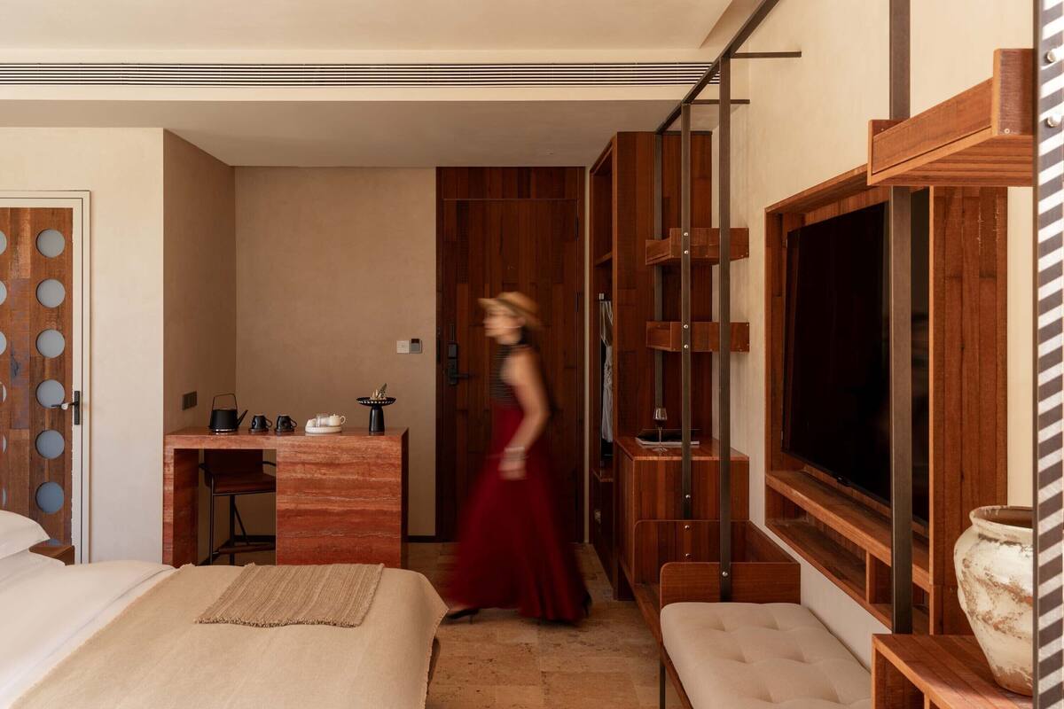 A modern hotel room with a bed, a desk, a TV, and a large window.