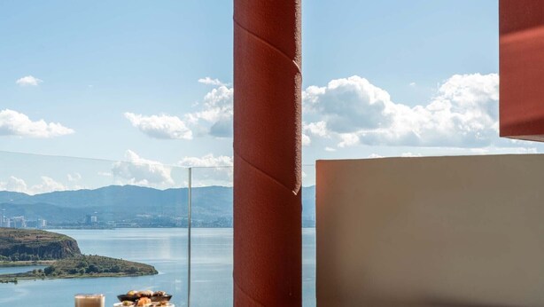 Une salle de bain moderne avec une grande baignoire, une table d’appoint en bois sur laquelle se trouve un verre d’eau, et une vue sur un lac avec des montagnes en arrière-plan.