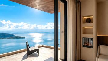 A balcony with a view of a body of water and distant land, a modern interior with a sofa and wall-mounted shelves, and a large window.