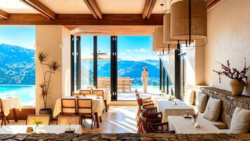A spacious room with a large window overlooking a mountainous landscape, furnished with tables and chairs.