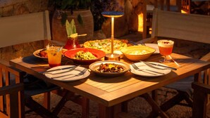 Un área de comedor al aire libre con una mesa lista para una comida, con vista a un cuerpo de agua y luces de la ciudad a lo lejos.