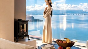 Una habitación con un ventanal grande con vistas a un cuerpo de agua, una mesa de madera con frutas, un sofá y una chimenea.
