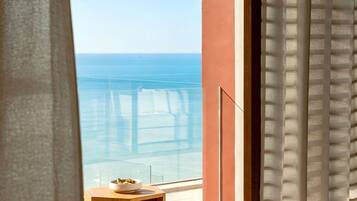 A balcony with a view of the sea, a small table with a bowl, and a window with curtains.