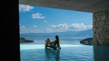 A person relaxing in a clear blue infinity pool with a cityscape and mountains in the background.