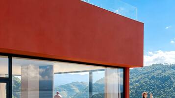 Un edificio moderno con ampie vetrate, facciata rossa e vista su un paesaggio montuoso.