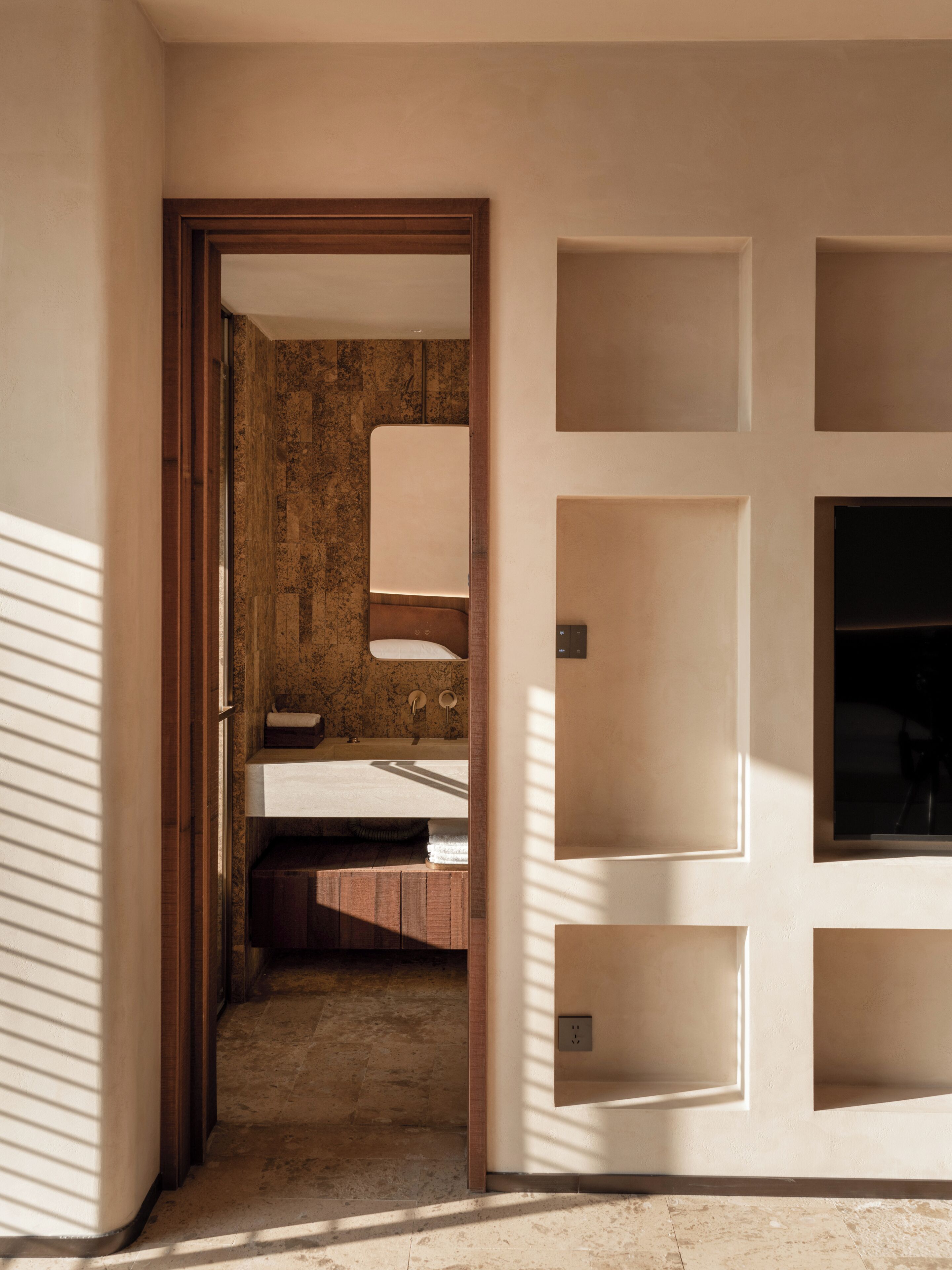 A hotel room with a wooden door, a bathroom with a sink and mirror, and a tiled floor.