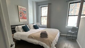 A bedroom with a bed, a ceiling fan, a window, and a chair.