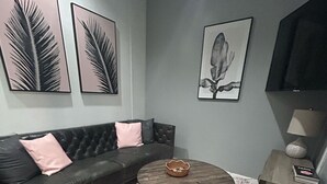 A living room with a dark leather sofa, a round wooden coffee table, a patterned rug, and wall art including palm leaves and a flower.