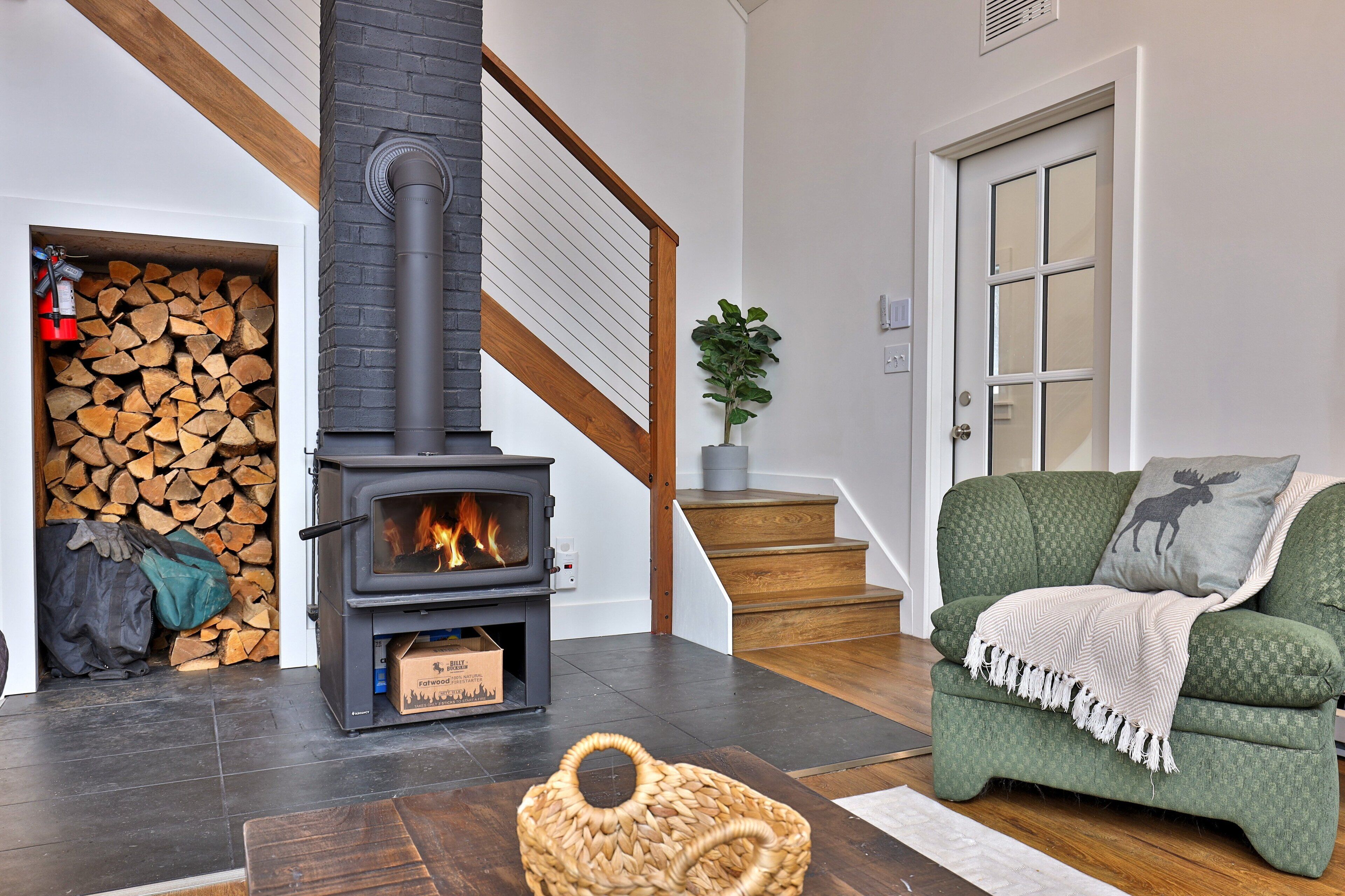 A living room with a fireplace, a green sofa, a wooden staircase, and a door with frosted glass panels.