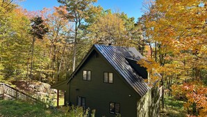 Ein grünes Haus mit geneigtem Dach, umgeben von Bäumen im Herbstlaub.