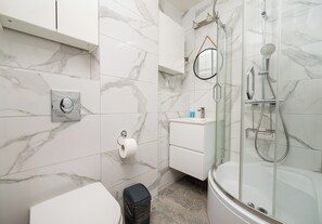 Et moderne badeværelse med en glasafskærmet bruseniche, toilet og vask med spejl over.