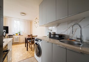 Et kompakt køkken med vaskemaskine, vask og spiseplads med en stol og et bord.