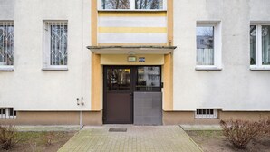 Ein Gebäudeeingang mit einer Doppeltür, einem kleinen Schild darüber und einem gepflasterten Weg zum Eingang.