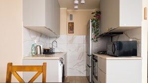 Eine kleine Küche mit Mikrowelle, Ofen und Spüle. Im Vordergrund steht ein Holzbstuhl und ein Tisch.