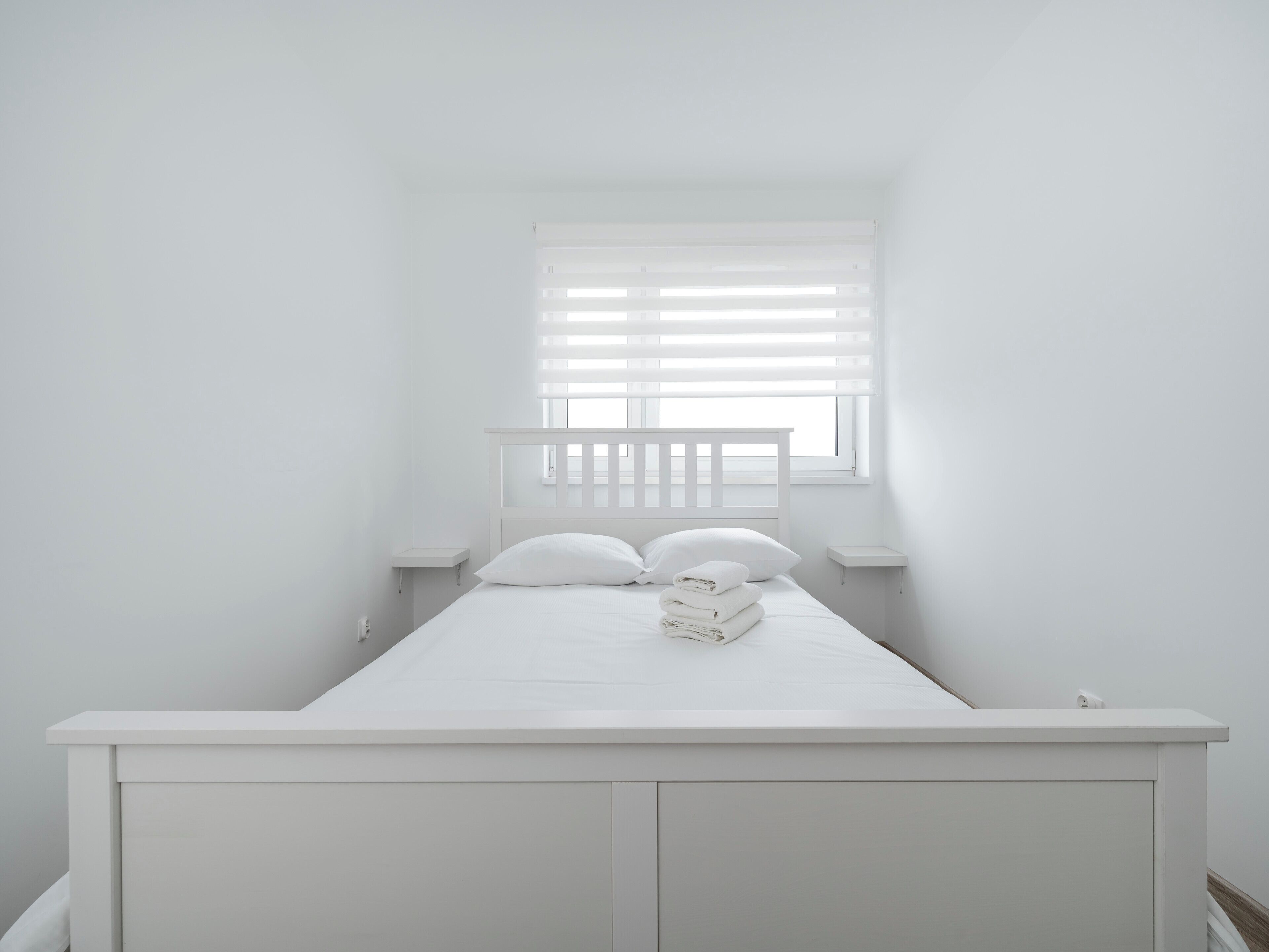 Une chambre individuelle avec un lit simple, dotée d’un plafond en pente, d’une fenêtre avec des stores et d’une petite table de chevet.
