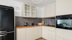 A modern kitchen with white cabinets, a black refrigerator, a Samsung oven, and a marble backsplash.