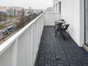 Un balcon doté d’un sol carrelé de carreaux noirs, de deux chaises en métal et d’une rambarde blanche.