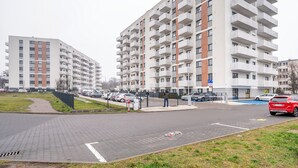 A multi-story residential building with balconies, a parking area, and a pedestrian pathway.