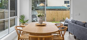 A dining area with a wooden table and chairs, a vase with flowers, and a grey sofa.