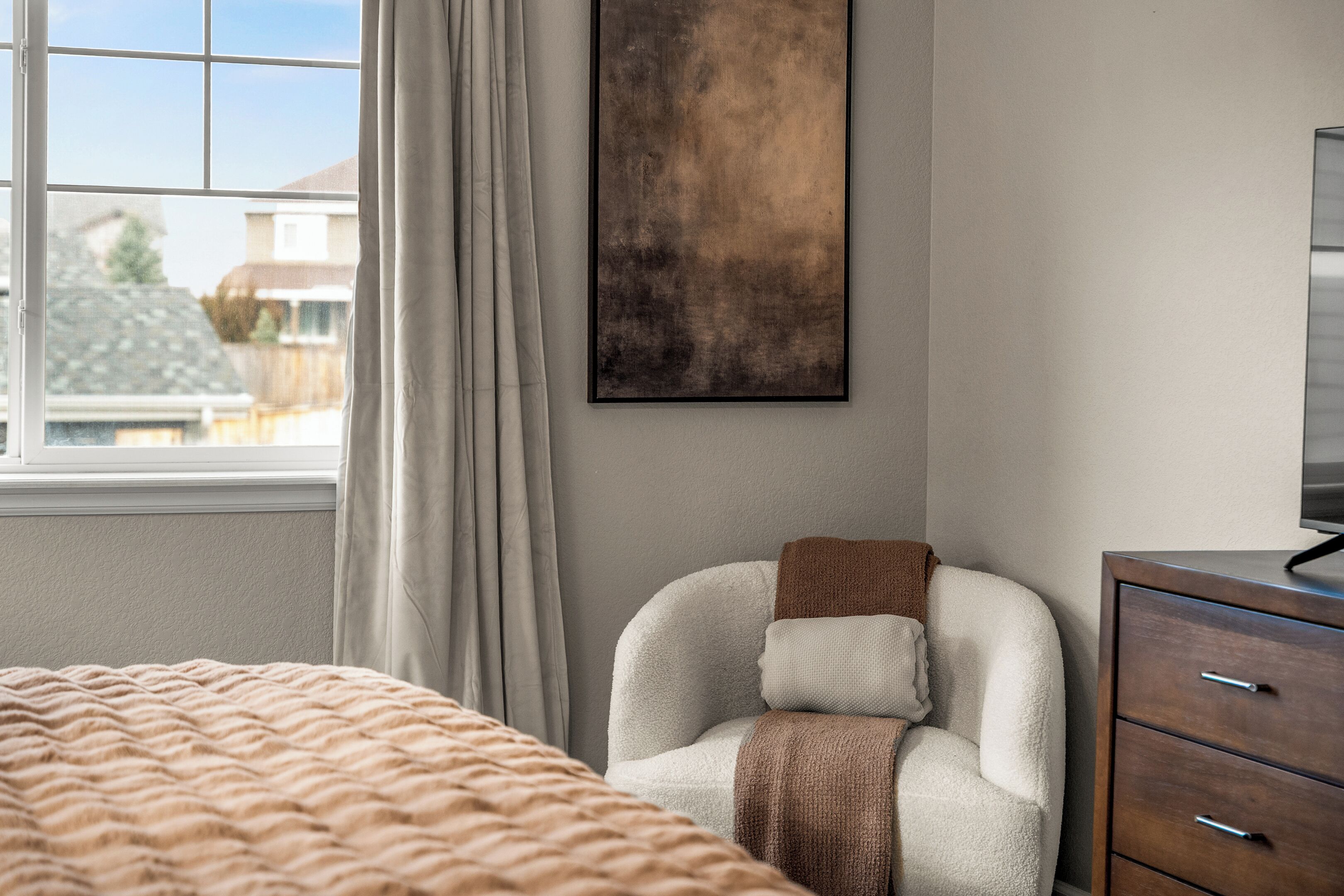 A bedroom with a bed, a chair, a dresser, and a window with curtains.