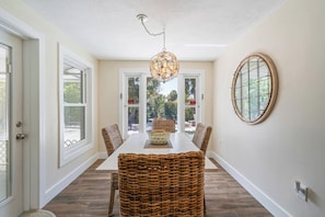 Un coin repas avec une table blanche, des chaises en osier et un luminaire suspendu.