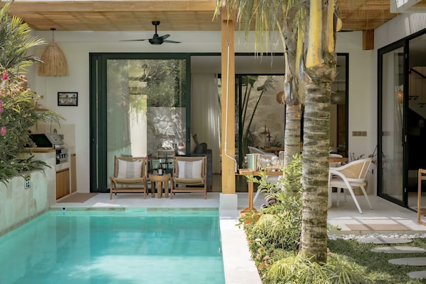 Zona de piscina con asientos, ventilador de techo y vista hacia el interior.