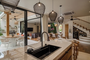 A modern kitchen with a large island, pendant lighting, and a view into the dining area. - Casa Mira Uluwatu (Uluwatu)