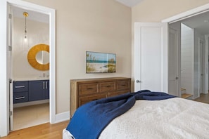 A bedroom with a bed, a dresser, a mirror, a painting, and a door leading to another room. - A Shore Thing: On Canal! Pool Spa!  Rooftop Deck by Anna Maria Life Vacation Rentals (Anna Maria)