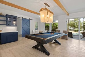 A pool table in a room with a wooden ceiling, a dining area, and a view of an outdoor swimming pool. - A Shore Thing: On Canal! Pool Spa!  Rooftop Deck by Anna Maria Life Vacation Rentals (Anna Maria)